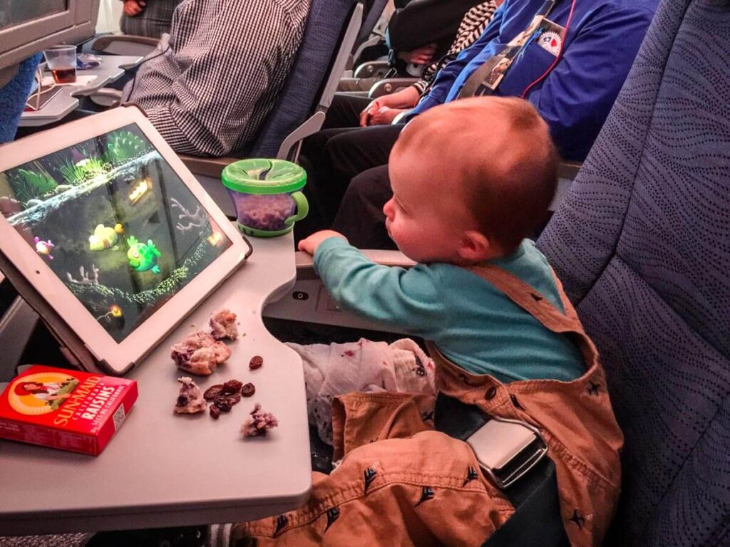 toddler on plane with ipad and planes snacks for toddlers on the tray table