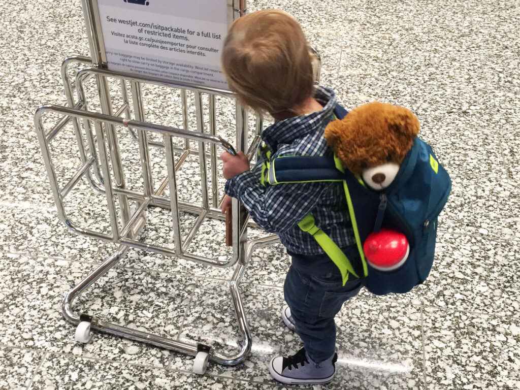 a toddler plays with a carry-on size checker at ther airport.