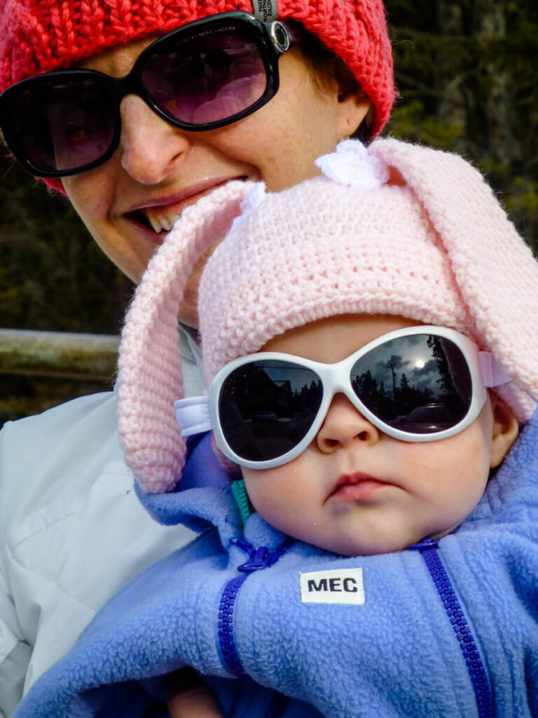 mother holding baby with pink hat and baby banz sunglasses