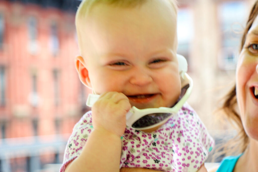 baby smiling and pulling off baby sunglasses strap