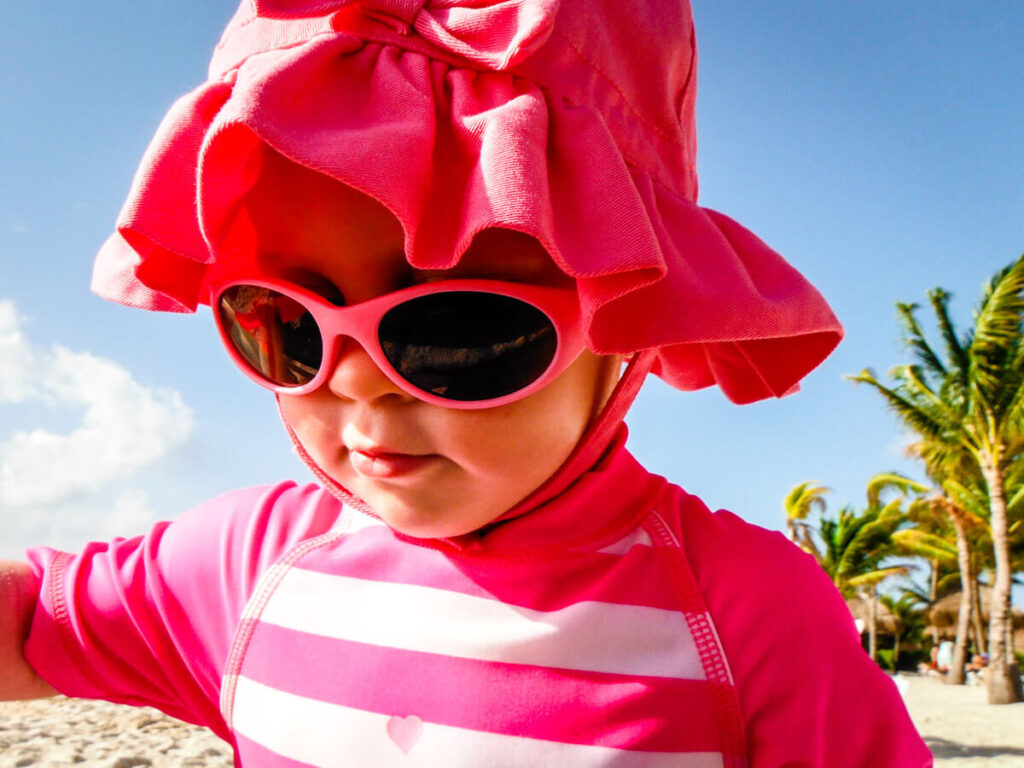 baby playing on beach wearing sunglasses.