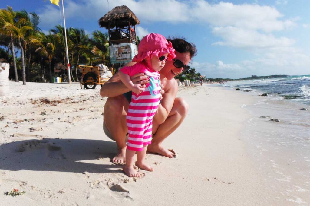 toddler wearing sunglasses standing on beach with mother.