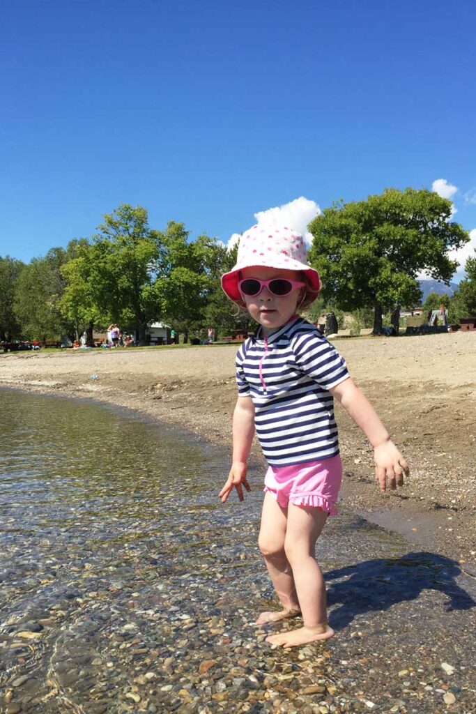 toddler in sunglasses standing in water.