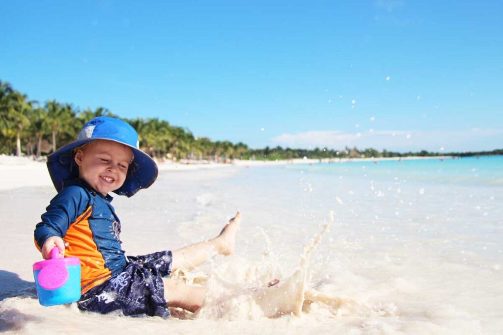 toddler boy in blue sun protection hat for toddlers splashing in ocean