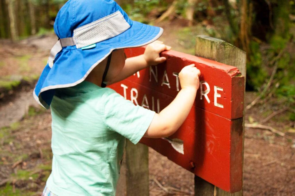 A toddler from the BabyCanTravel.com website, wears a blue, wide brim toddler sun hat while on a family hike.