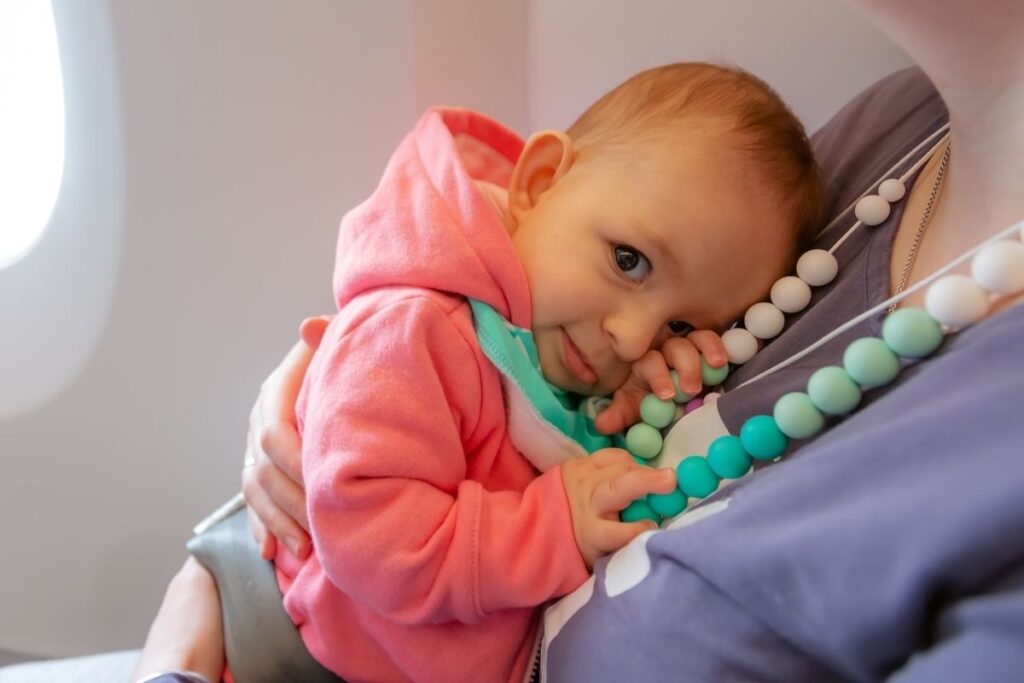 an infant holds on to a teething necklace while snuggling their mom on a flight together