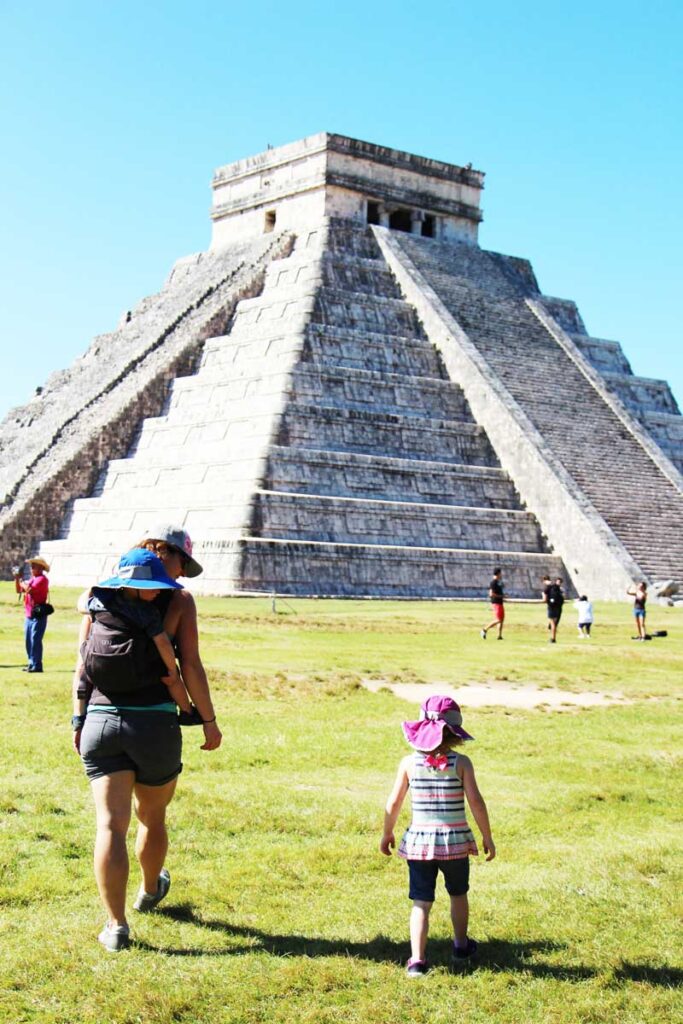 mother carrying toddler in back carrier walking with girl toddler in Mexico