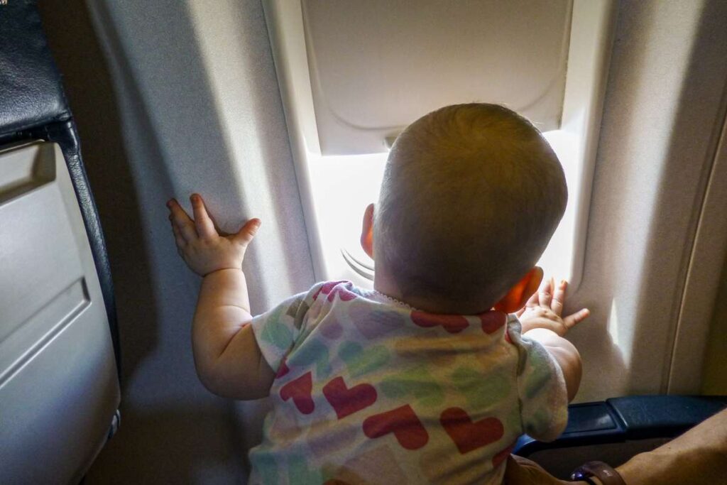 a baby looks out the airplane window on a 4 hour international flight