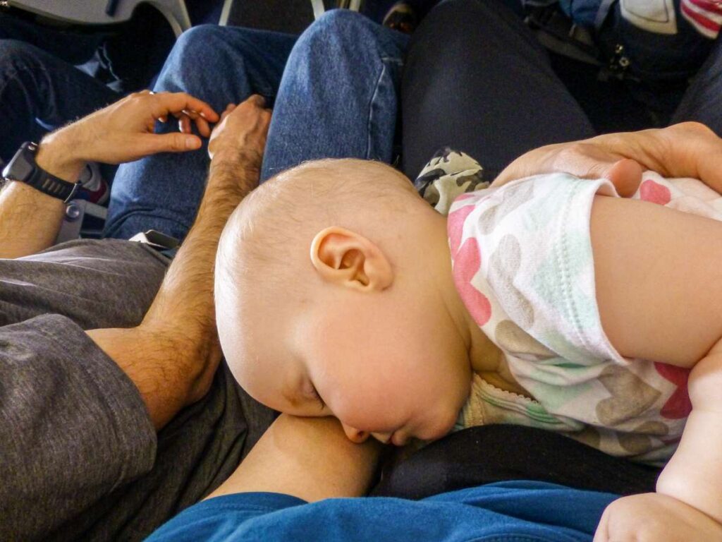 an infant sleeps on a plane while on her mom's lap