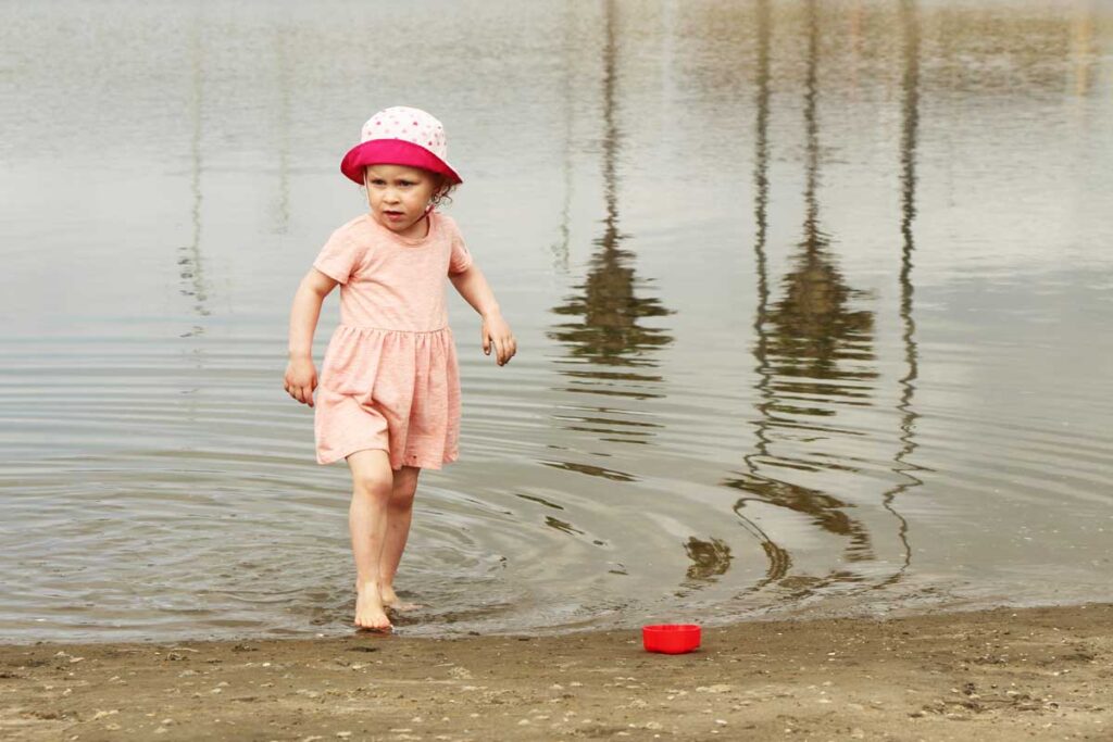 toddler girl in toddler bucket sun hat walking out of lake