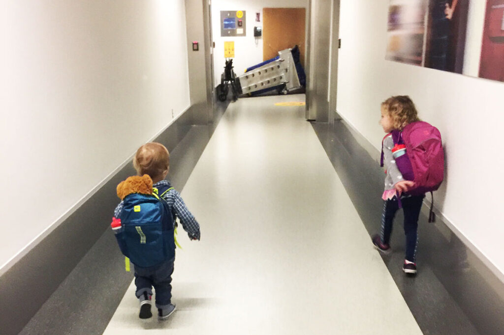 two toddlers walk along  hallway in an airplane before boarding  family flight.