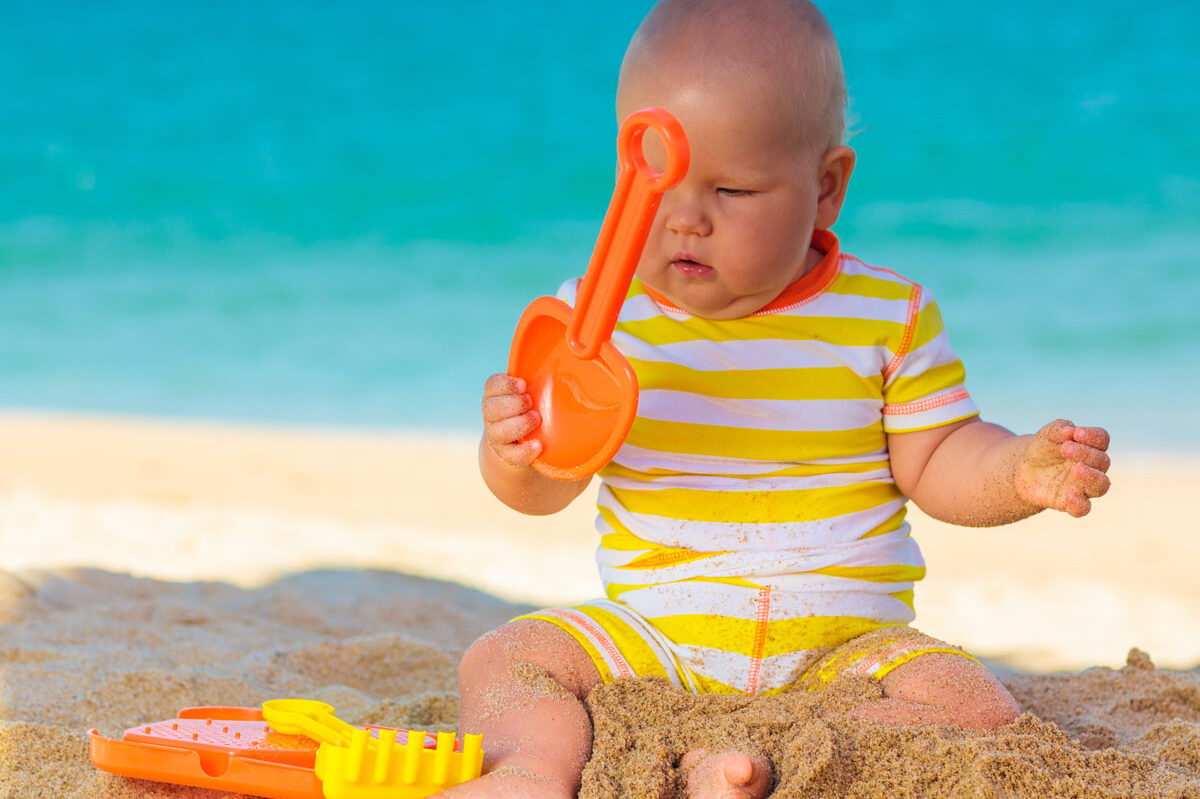 baby on beach playing with baby beach toys