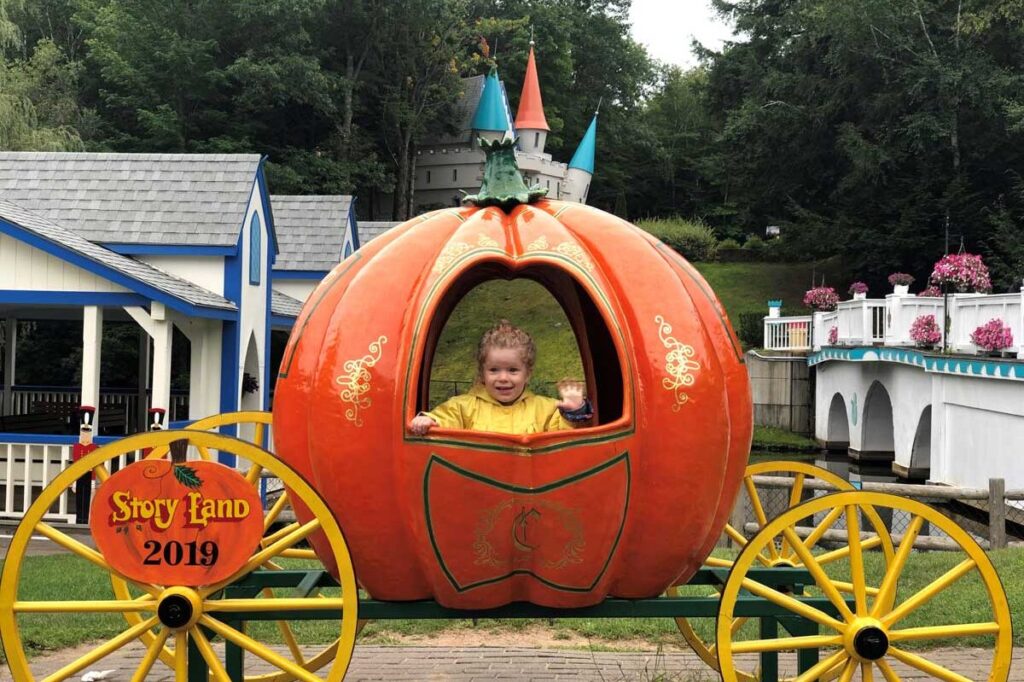 a toddler is all smiles within a pumpkin coach at Story Land