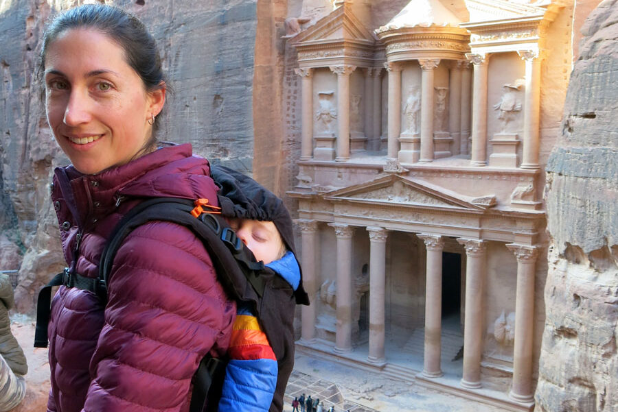 image of woman with baby in carrier on her back at Petra with the Treasury in background