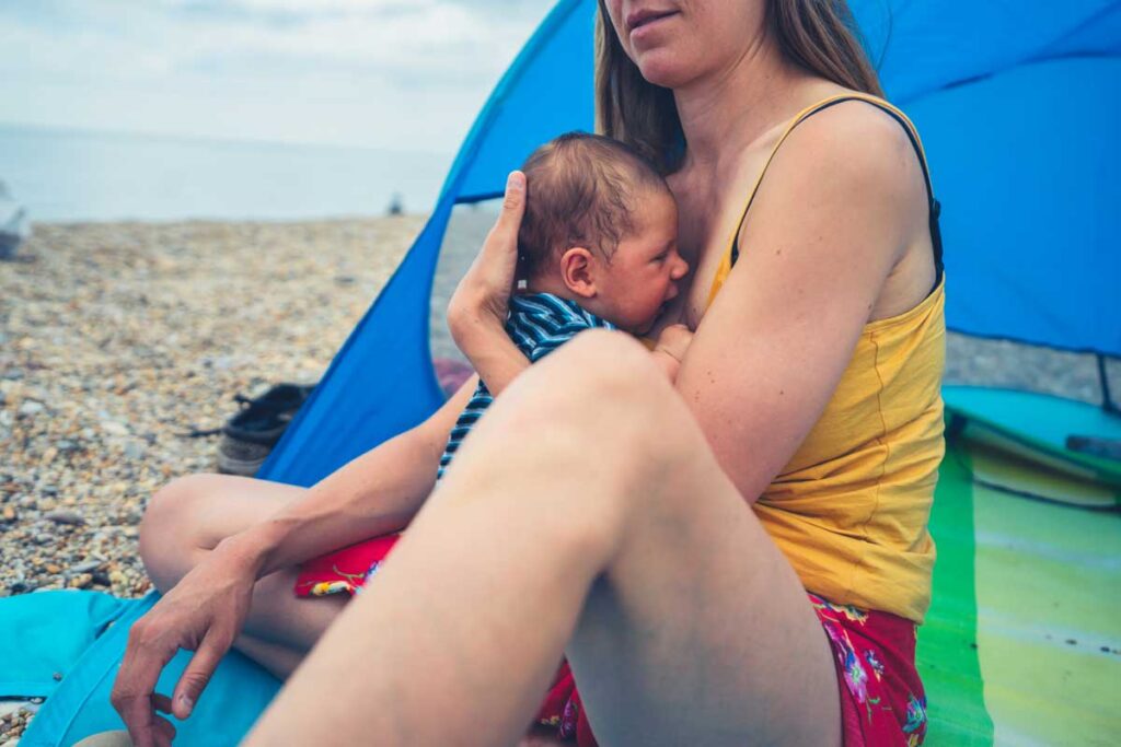 mother holding infant near beach tent - taking newborn to beach