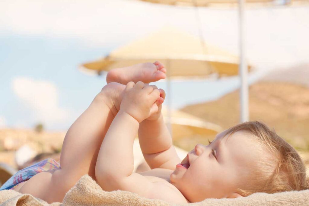 baby playing with toes laying on sand - taking baby to beach