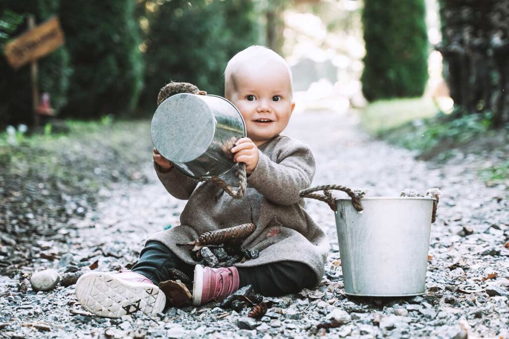 a baby sits on a pathway playing with pails.