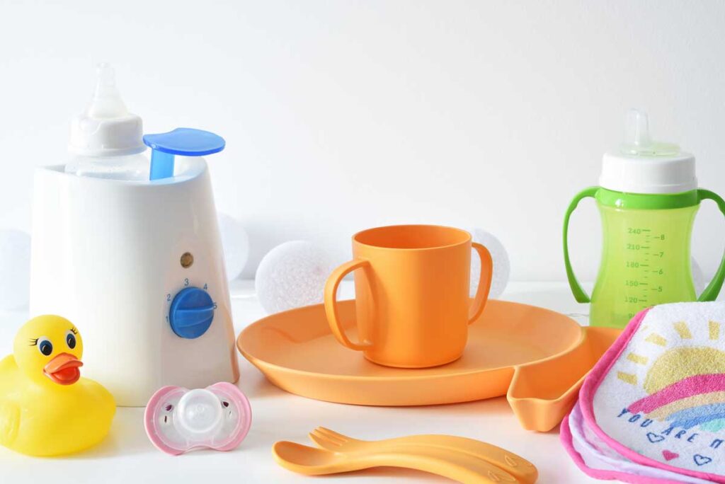 Travel Baby Food Warmer on counter with orange dishes and green sippy cup