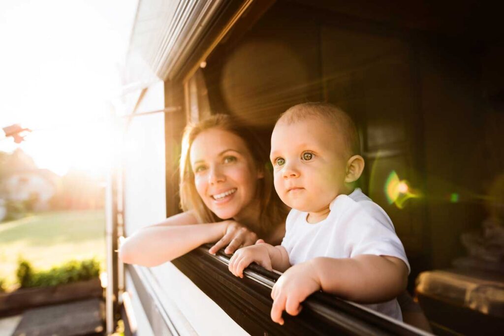 a baby and mother look out the window of their RV while camping.