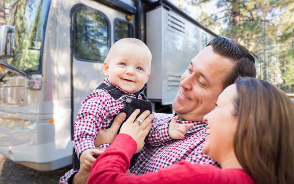 happy parents standing in front of RV holding baby.