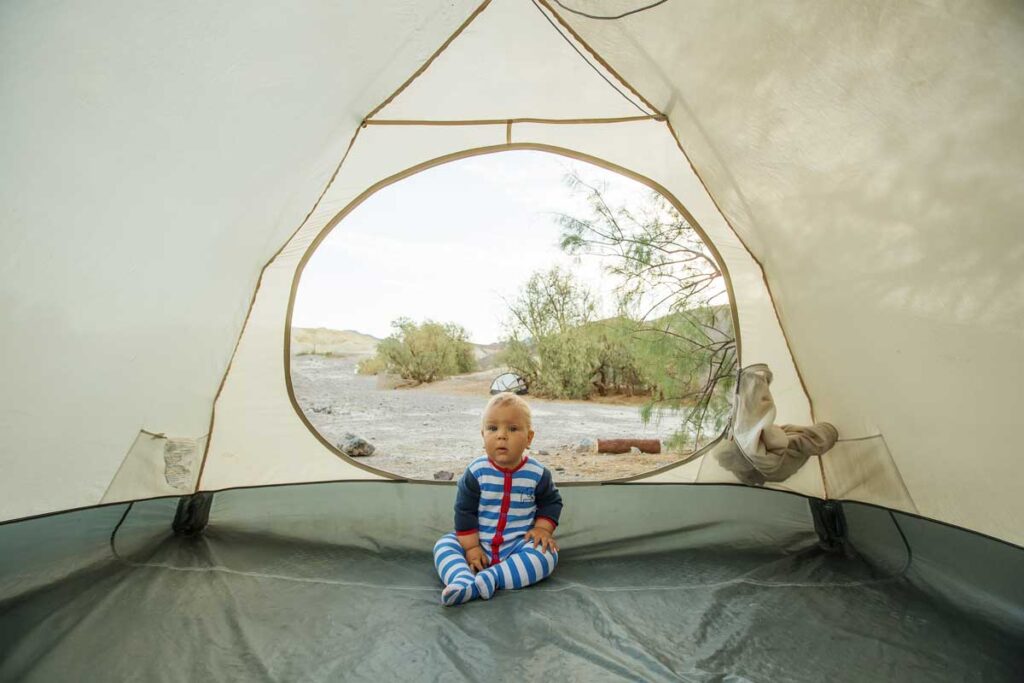 baby sitting in empty tent in footed pjs - camping with baby gear