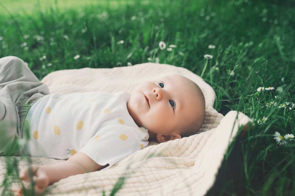 a baby lies on a blanket in the grass.