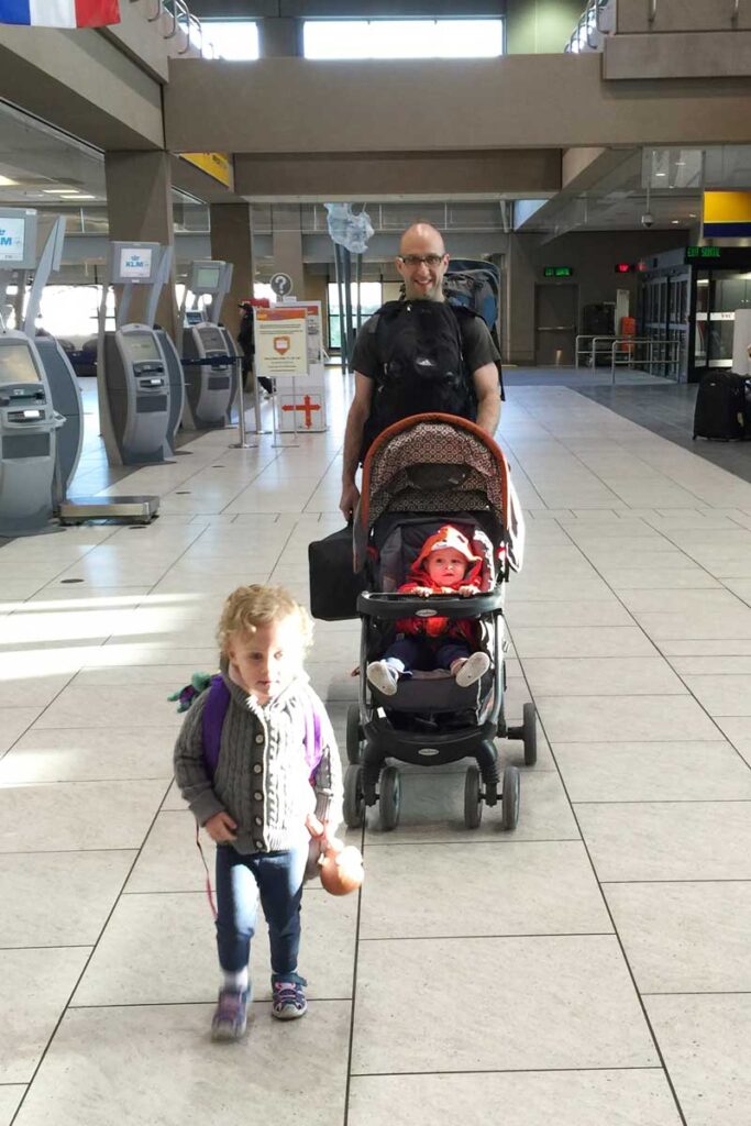 a father pushes his toddler with a stroller in the airport while his toddler runs ahead