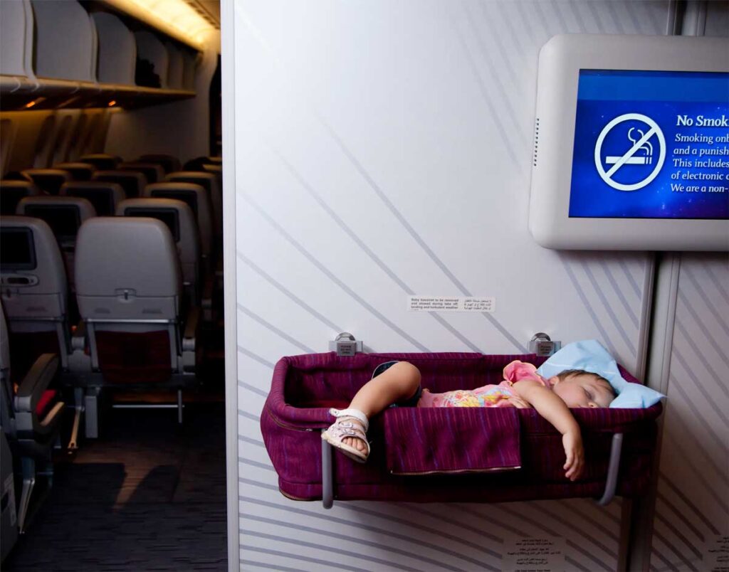 baby in airplane bassinet with arms and legs hanging out.