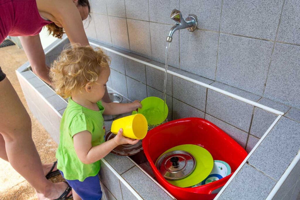 a toddler and mother washing dishes on a family camping trip.