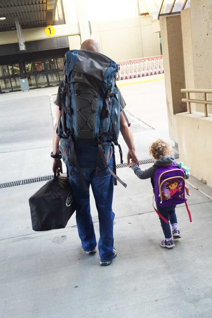 Dan Brewer, carries a pack n play into the airport, while holding his daughters hand.