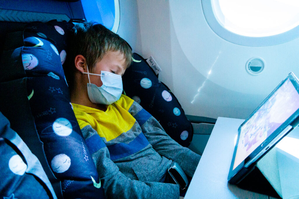 a child from the BabyCanTravel family uses the Seat to Sleep Travel Nest while on a long flight with his family.