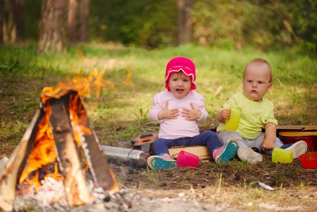 babies sitting near campfire with cups and dishes - camping gear for babies