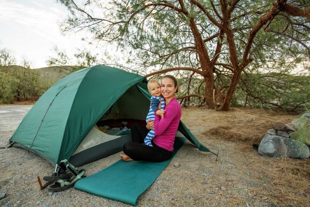 a mother holding a baby near a camping tent.