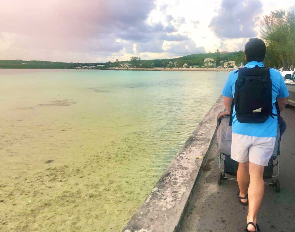 Father pushing stroller on ocean side path while wearing black travel backpack diaper bag