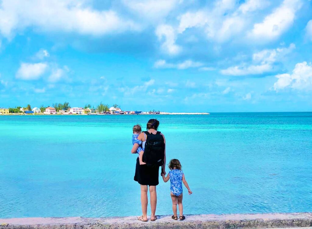 Mother with baby and toddler wearing No Reception Club diaper backpack standing in front of blue ocean