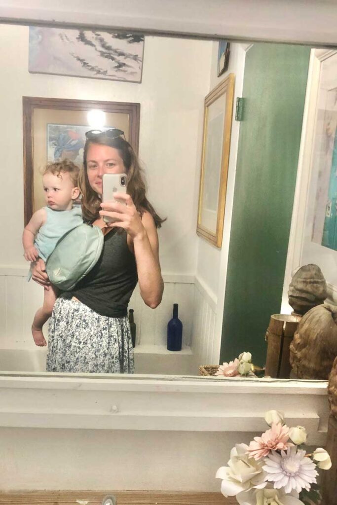 Woman in mirror holding baby and wearing Sidekick hip bag by No Reception Club