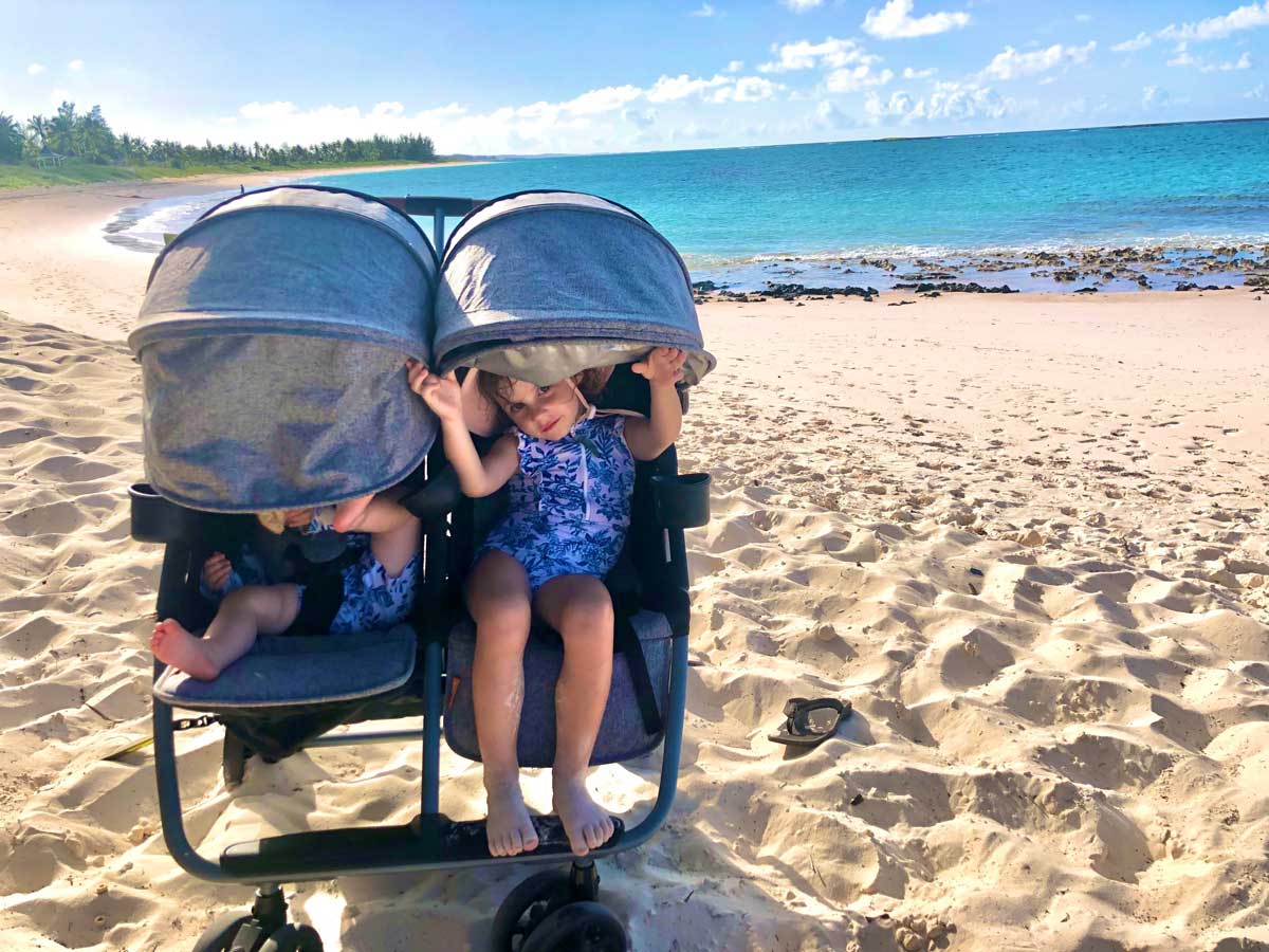 Zoe Twin Stroller on Beach with toddler peaking under canopy and baby in other seat