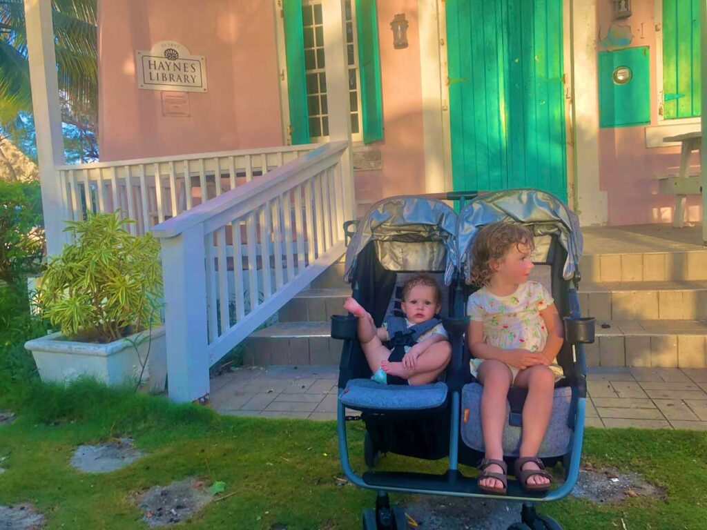 Toddler and baby sitting in Zoe Twin+ Stroller outside of house