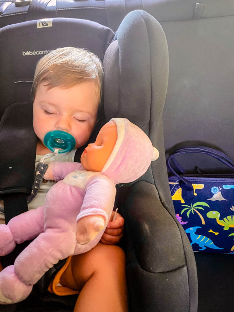 baby sleeping in travel car seat on road trip in Europe.