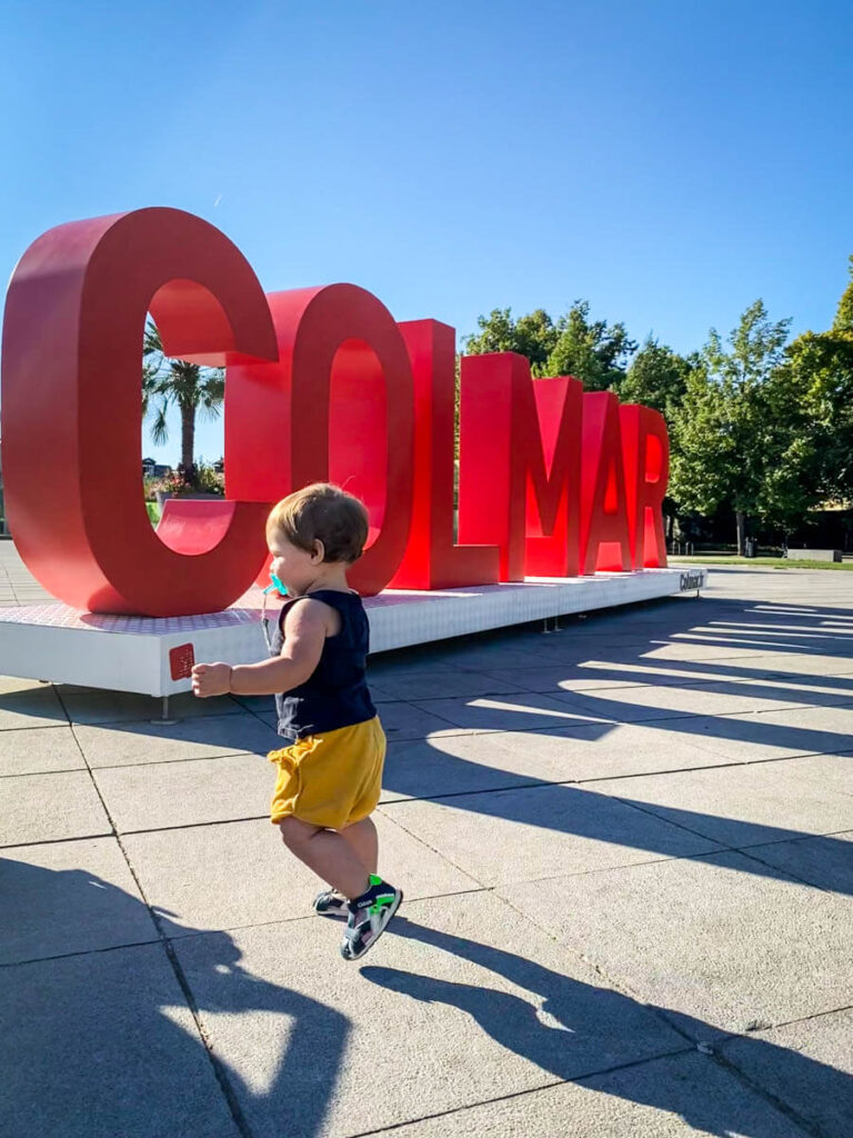 toddler running near Colmar sign while visiting Alsace France with a toddler.