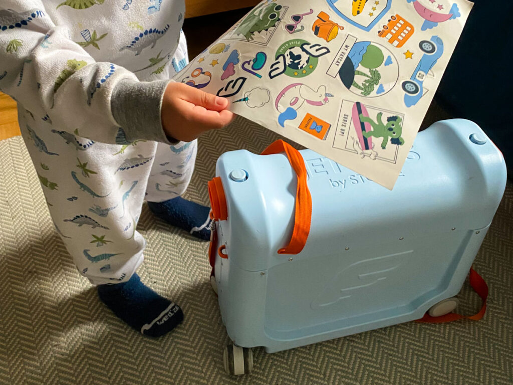 a toddler looks at travel stickers next to a blue JetKids BedBox by Stokke.