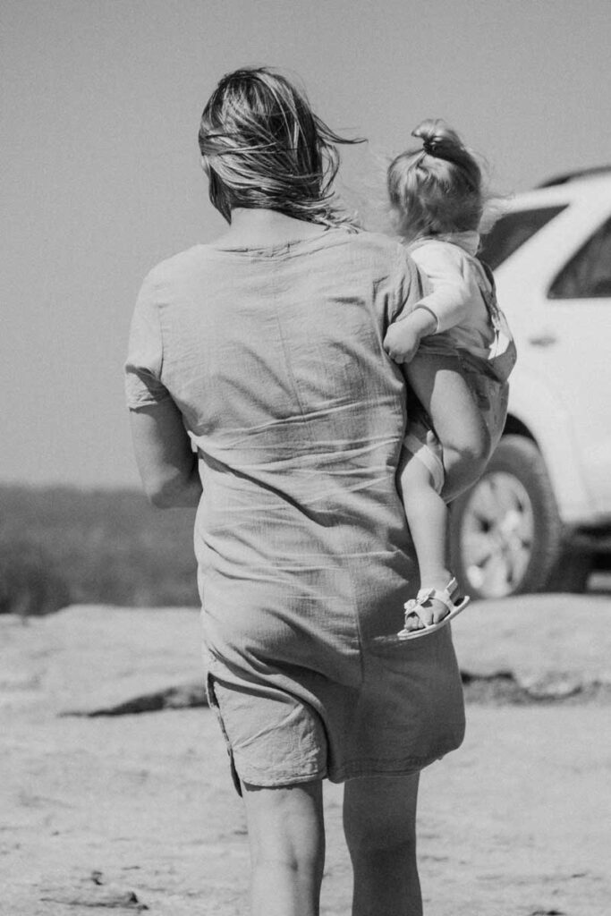 Woman carrying toddler back to car while on South African safari with toddler