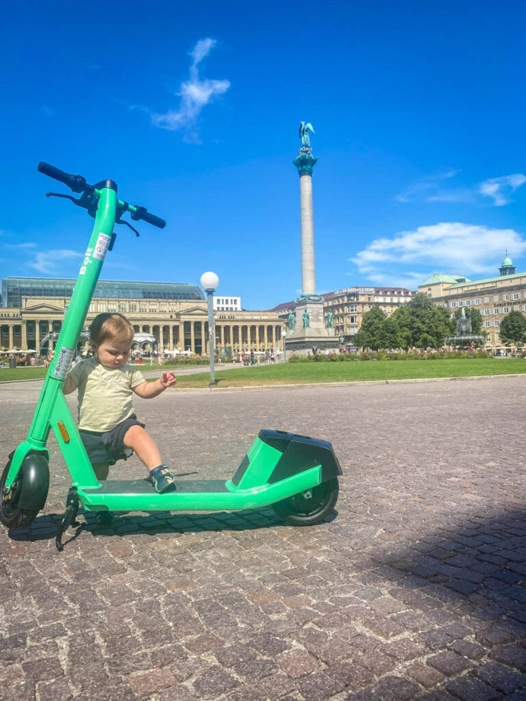 a toddler plays on a big green scooter in Stuttgart, Germany.