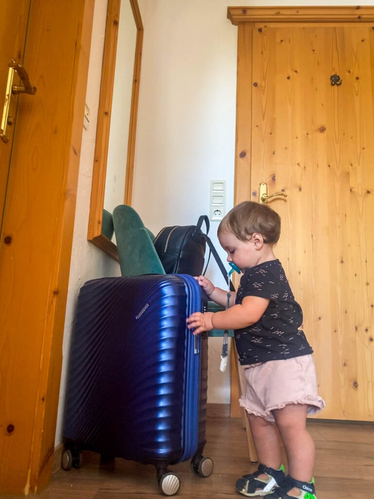 a 1 year old girl playing with suitcase before a family road trip with toddler.