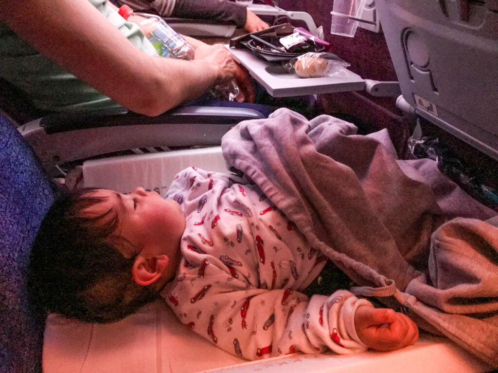 a toddler sleeps on a flight using a JetKids BedBox airplane bed.