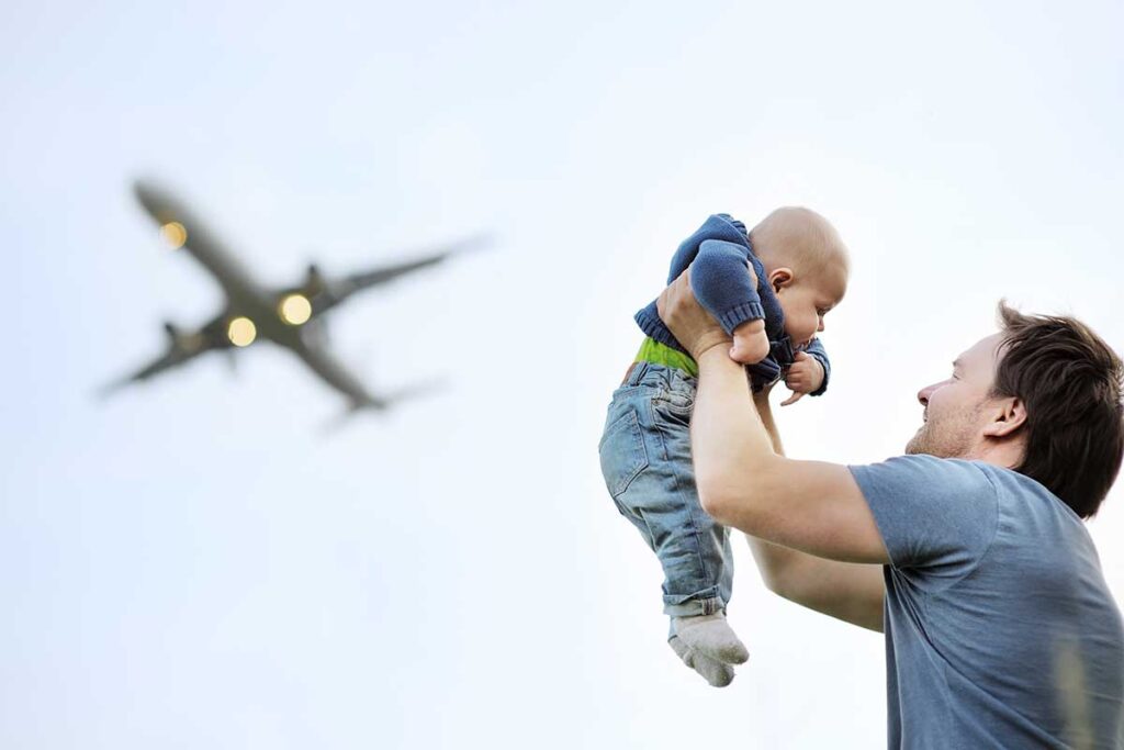 father holding baby in air with airplane flying overhead