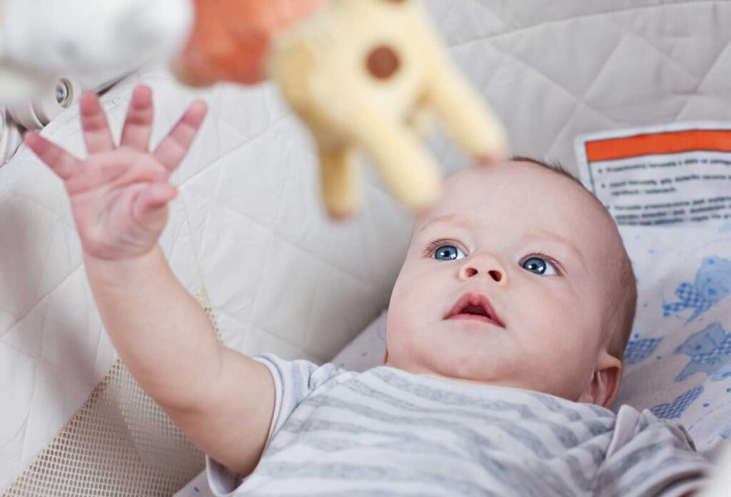 baby in travel crib playing with portable mobile