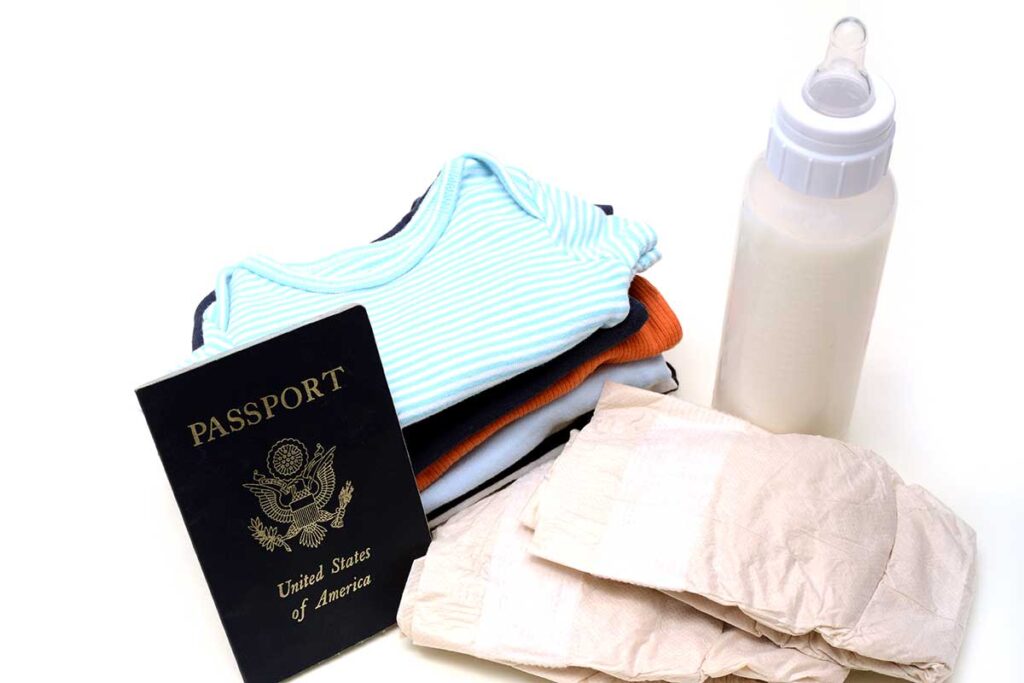 passport next to a pile of baby clothes, bottle and diapers.