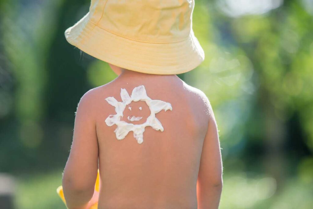 a child in a sun hat gets sunscreen put on while outdoors.