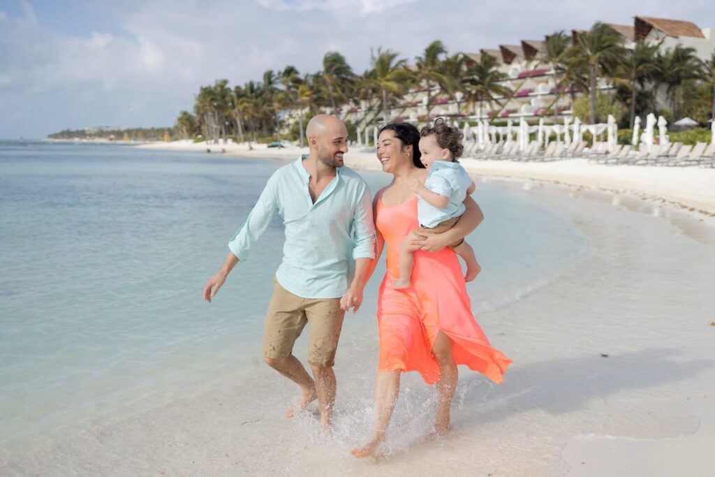 Happy parents go for a walk on the white sand beach with their baby at the Grand Velas Riviera Maya all-inclusive resort.